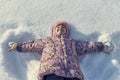 Little girl lying on her back in the snow, hand in hand in the form of an angel.