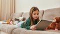 A little girl lying on her stomach holding a tablet on a sofa