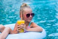 Little girl lying on inflatable ring in swimming pool. In the hands of a glass of mango juice. Holidays. Royalty Free Stock Photo