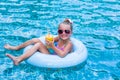 Little girl lying on inflatable ring in swimming pool. In the hands of a glass of mango juice. Holidays. Royalty Free Stock Photo