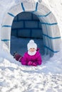 Little girl lying on the snow near the entrance to igloo.