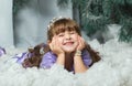 Little girl lying in the snow and smiling at the background of a fur-tree, photosession Studios. new year2018, Christmas