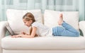 Little girl lying on sofa looks at notebook and laughs Royalty Free Stock Photo