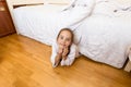 Little girl lying under bed at home and looking at camera Royalty Free Stock Photo