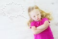 Little girl lying on white wooden floor with a speech bubble above her head Royalty Free Stock Photo