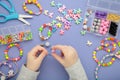 Little girl made bracelets on purple background. Kids handmade beaded jewelry. DIY bracelet beads