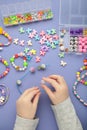 Little girl made bracelets on violet background. Kids handmade beaded jewelry. DIY bracelet beads