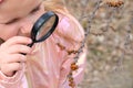 Little girl with a magnifying glass in her hand investigate details of spring nature . Springtime outdoor kids activity and