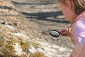 Little girl with a magnifying glass in her hand investigate  details of stone covered with moss or algae . Springtime outdoor kids Royalty Free Stock Photo