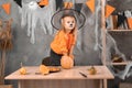 A little girl makes a jack-o-lantern out of a large pumpkin to celebrate Halloween. Witch costume, hat and makeup. take