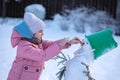 Little girl makes snowman on winter frosty day. Child makes nose out of carrot. Royalty Free Stock Photo