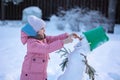 Little girl makes snowman on winter frosty day. Child makes nose out of carrot. Royalty Free Stock Photo