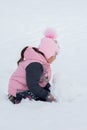 Little girl making big snow ball for constructing snow man in park in daytime with ground covered with snow in Royalty Free Stock Photo