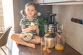 Little girl making fresh juice sitting on the table in home kitchen Royalty Free Stock Photo