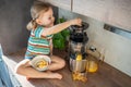 Little girl making fresh juice sitting on the table in home kitchen Royalty Free Stock Photo
