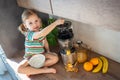 Little girl making fresh juice sitting on the table in home kitchen Royalty Free Stock Photo