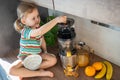 Little girl making fresh juice sitting on the table in home kitchen Royalty Free Stock Photo