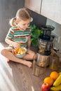 Little girl making fresh juice sitting on the table in home kitchen Royalty Free Stock Photo