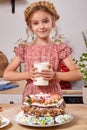 Little girl is making a homemade cake with an easy recipe at kitchen against a white wall with shelves on it.