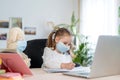 Little girl in mask, with Teddy bear, doing homework, e-learning Royalty Free Stock Photo