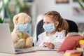 Little girl in mask, with Teddy bear, doing homework, writing in notebook Royalty Free Stock Photo