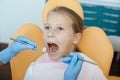 Little girl in medical chair opens her mouth, dentist in rubber gloves with tools treats teeth or put filling