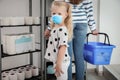 Girl with medical mask and mother buying toilet paper in shop