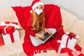 Little girl in a medical mask  santa claus hat uses a laptop while sitting on the sofa at home for christmas Royalty Free Stock Photo