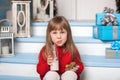 Merry Christmas! New Year. Little girl with milk and a gingerbread man sitting on porch near house. Royalty Free Stock Photo