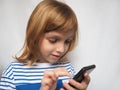 Little girl with mobile phone in her hands. Studio shot. The girl pokes her finger at the smartphone and smiles. Child with blond