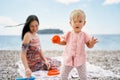 Little girl with a mold in her hand stands on a pebble beach against the background of a smiling mother Royalty Free Stock Photo