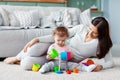 Little girl and mom play on the floor on a light carpet with bright toys, build a tower