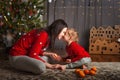 Little girl and mom in a red sweater with a deer for the New Year. Girl and sister at Christmas tree at home with tangerines. The