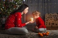 Little girl and mom in a red sweater with a deer for the New Year. Girl and sister at Christmas tree at home with tangerines. The