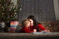 Little girl and mom in a red sweater with a deer for the New Year. A girl and a sister are reading a book by the Christmas tree at