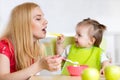 Little girl and mother with baby food feeding each other, sitting at table in nursery Royalty Free Stock Photo