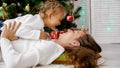 Little girl and mother hugging indoors with christmas tree on the background. Royalty Free Stock Photo