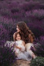 A little girl and mother with long flowing hair are sitting among the bushes in a lavender field in puffy tulle dresses