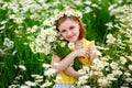 A little girl in nature with a wreath of daisies from flowers on her head and a bouquet in her hands. Field of camomiles on a Royalty Free Stock Photo