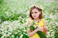 A little girl in nature with a wreath of daisies from flowers on her head and a bouquet in her hands. Field of camomiles on a Royalty Free Stock Photo