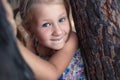 A little girl near a pine tree shows a wobbly baby tooth in her mouth