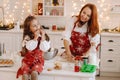A little girl in the New Year& x27;s kitchen is sitting on the table with cookies in her hands eating it, and her mother is Royalty Free Stock Photo