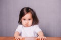 Little girl offended, little girl sitting at table in white T-shirt on gray background