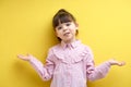 little girl with open hands asking sorry, isolated on yellow background. Oops.