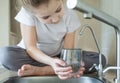 Little girl open a water tap with her hand holding a transparent glass. Kitchen faucet. Filling cup beverage. Pouring fresh drink Royalty Free Stock Photo