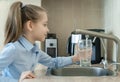 Little girl open a water tap with her hand holding a transparent glass. Kitchen faucet. Filling cup beverage. Pouring fresh drink