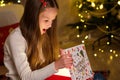Little girl opening Christmas gift on background of Christmas Tree at home Royalty Free Stock Photo