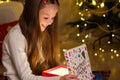 Little girl opening Christmas gift on background of Christmas Tree indoors Royalty Free Stock Photo