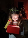 a little girl opens a box with a gift and is very happy with a surprise on Christmas evening near the New Year tree Royalty Free Stock Photo