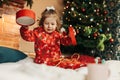 A little girl opens a Christmas present near the Christmas tree. Christmas time, gifts, festive mood. The concept of Royalty Free Stock Photo